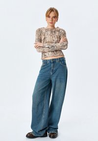 Top a maniche lunghe con stampa pitonata e orlo corto, abbinato a jeans in denim blu a gamba larga. Modella che indossa scarpe con plateau nere.