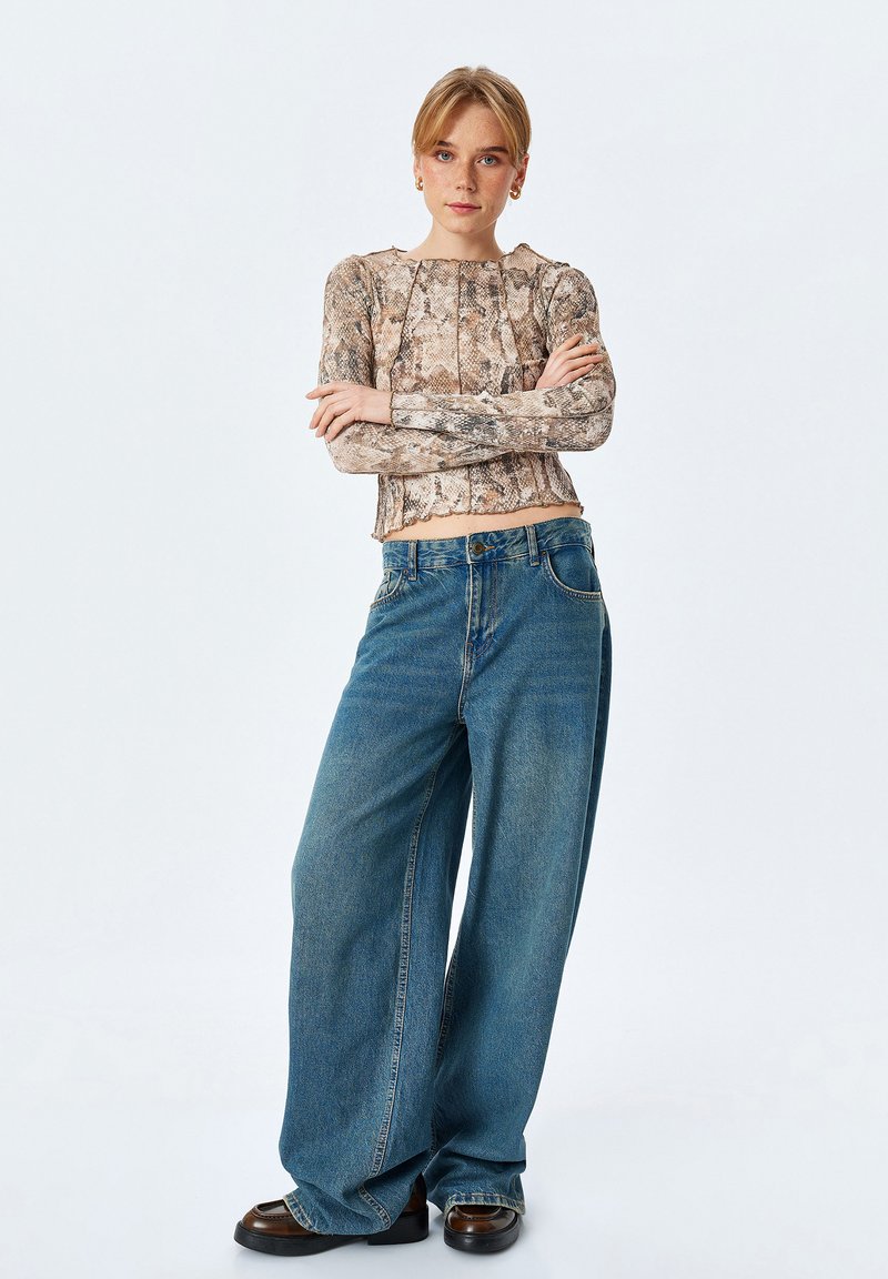 Top a maniche lunghe con stampa pitonata e orlo corto, abbinato a jeans in denim blu a gamba larga. Modella che indossa scarpe con plateau nere.