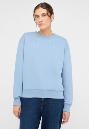 Sweat-shirt bleu clair avec le texte "MUSTANG" en relief. Présente un col rond, des poignets côtelés et une coupe décontractée. Associé à un jean bleu foncé.