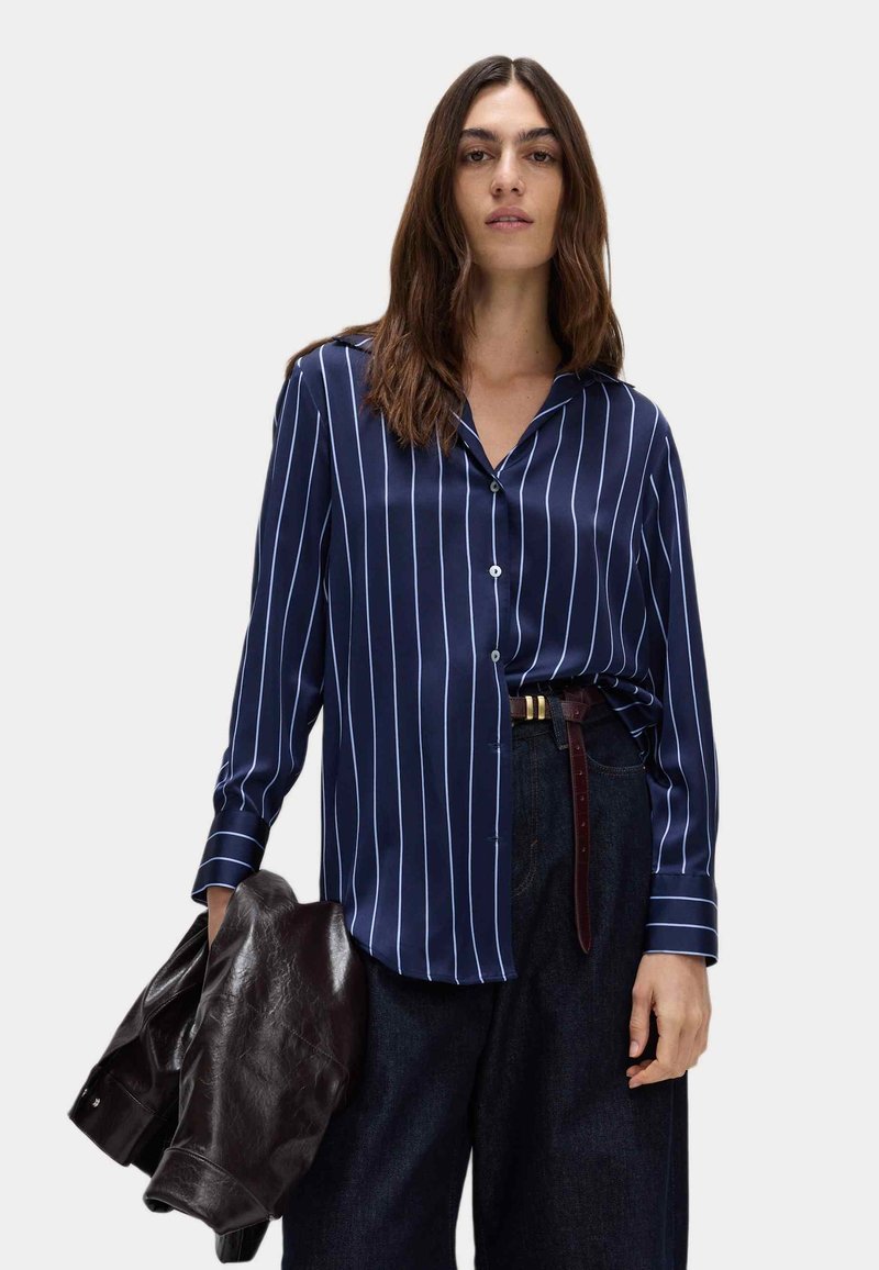 Camicia a strisce navy a maniche lunghe in tessuto morbido, con righe verticali bianche, chiusura con bottoni sul davanti e vestibilità rilassata, abbinata a pantaloni di jeans.