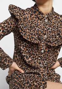 Klänning i leopardmönster med volangkrage, knappstängning, långa ärmar och mjukt tyg med glansiga detaljer.