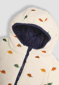 Felpa bianca in pile con motivi di dinosauri multicolori in verde, arancione e marrone. Fodera in blu navy trapuntata, chiusura con zip a tutta lunghezza.