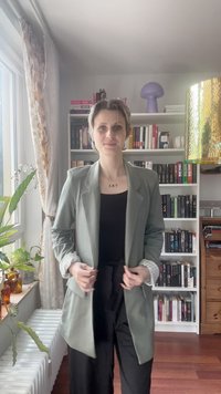 Blazer su misura verde chiaro con collarino a revers, tessuto strutturato e dettagli a righe sui polsini, abbinato a una maglietta nera e pantaloni neri larghi.