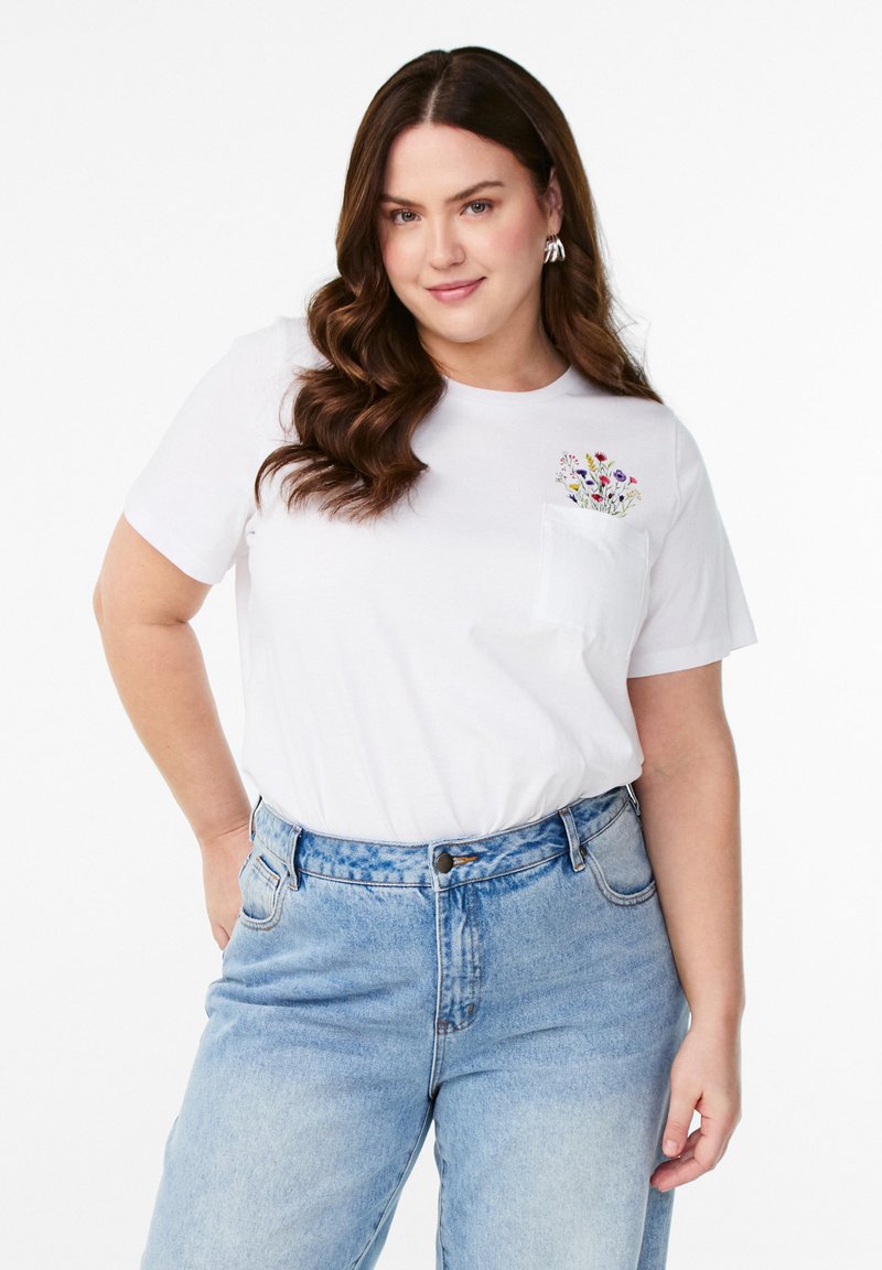 Bílý bavlněný tričko s krátkými rukávy a kapsou na hrudi, který má barevné květinové vyšívání; spojené se světle modrými džíny s vysokým pasem.