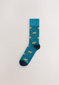 Chaussettes turquoise avec une bordure côtelée et un bout de pied marine. Présentent des motifs de lions jaunes partout. Construites dans un tissu lisse et extensible.
