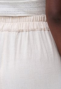 Lichtbeige, geweven stof met een elastische tailleband, met subtiele patronen. Close-up van kledingdetails, die het materiaal en het ontwerp benadrukt.