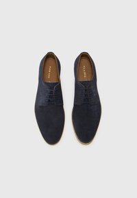 Chaussures en daim bleu marine à lacets avec une texture lisse, bout arrondi et doublure intérieure marron contrastante. Remarquables par leur design minimaliste et leurs accents subtils.