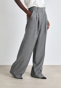 Harmaat raidalliset housut, joissa on laskokset, korkea vyötärö ja sivutaskut. Kangas on sileäpintaista ja siinä on hienovarainen kiilto.