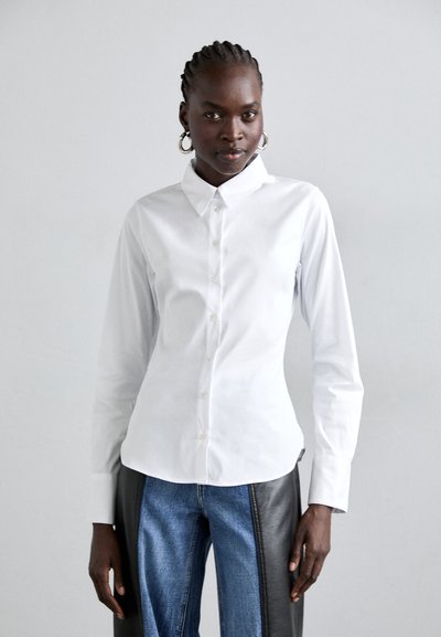 Chemise blanche à col classique, à manches longues et au toucher lisse. Associée à un jean bleu avec des accents en cuir noir.