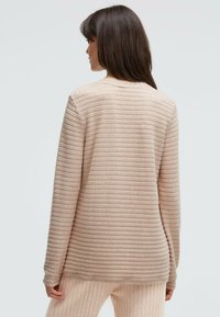 Hellrosa gestreifter Pullover aus weichem Material. Verfügt über einen Rundhalsausschnitt und lange Ärmel mit entspanntem Schnitt. Durchgehend horizontale, gerippte Struktur.