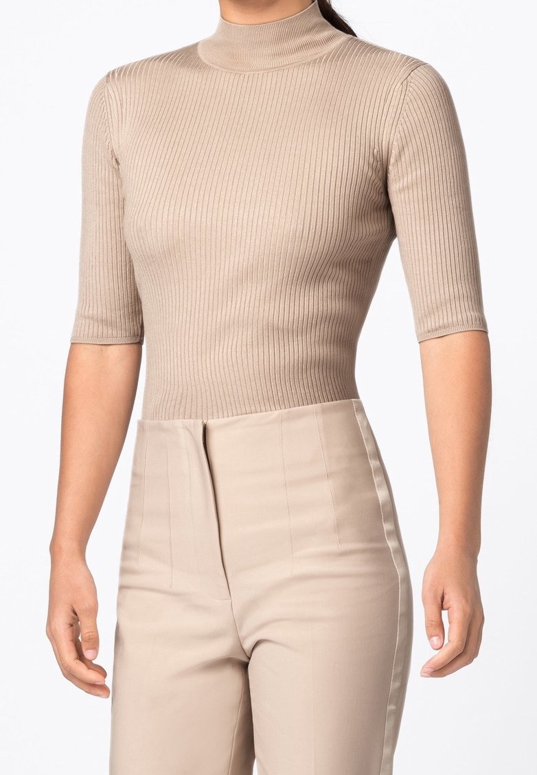Prążkowana, krótki rękaw bluzka w beżowym kolorze z wysokim dekoltem, w połączeniu z spodniami w wysokim stanie w beżowym kolorze, z wyraźnymi szwami i gładką fakturą.