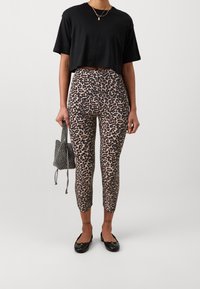 Black cropped t-shirt with short sleeves, paired with beige leggings featuring a black leopard print. Worn with black flats and a small patterned bag.