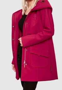 Veste imperméable fuchsia, à capuche avec une fermeture éclair frontale, des boutons-pression, une grande poche latérale et un logo discret. Texture lisse.