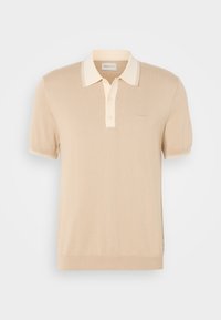 Ανοιχτό μπεζ πόλο μπλούζα φτιαγμένη από μαλακό πλεκτό ύφασμα. Διαθέτει αντίθεση στον γιακά και πλαίσιο με δύο κουμπιά. Διακριτική σήμανση στο στήθος.