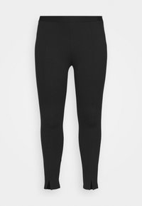 Leggings noirs en tissu extensible, présentant une texture lisse, une forme fuselée et de petites fentes au niveau de la cheville. Design minimaliste.