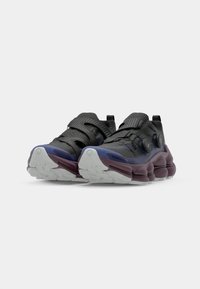 Des chaussures de sport noires avec une finition texturée, des sangles ajustables et une semelle rembourrée teintée de violet. Présentent une forme unique et un profil de semelle prononcé.