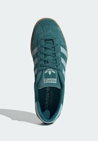 Teal suede sneaker with three white stripes on sides, lace-up closure, padded tongue, and rubber gum sole. Branding on tongue and insole.
