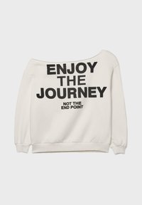 Felpa bianca con design off-shoulder, caratterizzata da testo nero: "GODITI IL VIAGGIO" e "NON IL PUNTO DI ARRIVO." Tessuto morbido e texture.