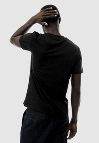 T-shirt nero a maniche corte con collo rotondo, design aderente, trama di tessuto morbida e vista posteriore liscia. Indossato con jeans in denim scuro.