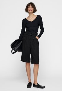 Zwarte geribbelde lange mouw top en zwarte knielange shorts met een trekkoord in de taille, gecombineerd met een grote zwarte handtas en platte schoenen.