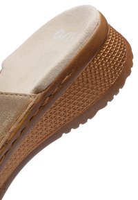 Beige ruskinds kile-sandal med tekstureret brun sål og polstret fodseng, vinklet for at vise sidesting og sålmønster.