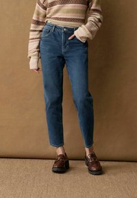 Blauwe high-waisted spijkerbroek van denim, met een rechte pijp. In combinatie met donkerbruine platform loafers. Gewaxt stof.