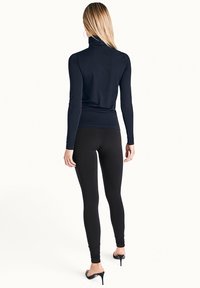 Svart polotröja med långa ärmar och svarta leggings. Slim fit, slät textur. Modellen bär högklackade skor. Enkel, klassisk design.