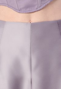 Top corto lilla con una texture satinata liscia, dotato di cuciture curve. Abbinato a pantaloni a vita alta lilla coordinati che mostrano linee pulite.