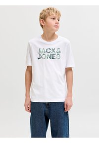 Ξανθό αγόρι που φοράει λευκό μπλουζάκι Jack & Jones με πράσινο μοτίβο φύλλων, συνδυασμένο με φαρδιά μπλε τζιν, κοιτάζοντας προς τα πλάγια.