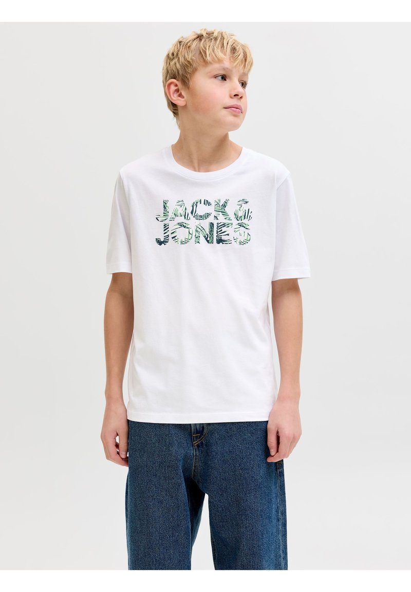 Ξανθό αγόρι που φοράει λευκό μπλουζάκι Jack & Jones με πράσινο μοτίβο φύλλων, συνδυασμένο με φαρδιά μπλε τζιν, κοιτάζοντας προς τα πλάγια.