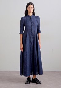 Navy blue long dress with a button-up front, three-quarter sleeves, and a flared silhouette. Worn with black lace-up shoes.