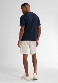 Námořnické bavlněné tričko s krátkým rukávem, kulatým výstřihem a bílým prošitím, spojené se světle béžovými šortkami a bílými teniskami.