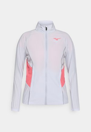 Bílá sportovní bunda s růžovými bočními panely, vysokým límcem, dlouhými rukávy a zapínáním na zip, vyrobená z lehkého, prodyšného materiálu.