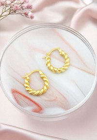 Vriden guldmetallringörhängen som visas på en marmoryta med rosa och vita nyanser; slät textur och cirkulär form.