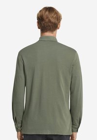 Långärmad, olivgrön polo tröja med krage, sidoflikar och knappr detaljer vid ärmsluten, tillverkad av mjukt, texturerat tyg.