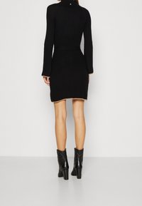Musta, vartalonmyötäinen pitkähihainen mekko, jossa on teksturoitu kuvio, korkea kaula-aukko ja kontrastiväriset beigen väriset reunat. Yhdistetty mustiin korkokenkiin ankle boots.