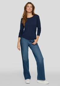 Marineblauer Strickpullover mit rundem Ausschnitt, kombiniert mit blauen Jeans mit weitem Bein und weißen Sneakers. Der Pullover hat gerippte Bündchen und Saum.