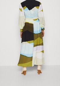 Pitkä mekko sekoitetuissa pastelliväreissä, jossa abstrakteja maisemakuoseja, vartalonmyötäinen vyötärö, liehukehihat ja napilliset kalvosimet. Sileä kangas ja virtaava design.