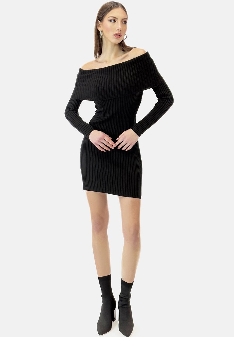 Schwarzes geripptes Off-Shoulder-Kleid mit langen Ärmeln, figurbetonter Passform und mini Länge. Kombiniert mit schwarzen High-Heel-Stiefeletten.