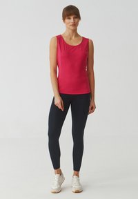 Top atletico rosa aderente senza maniche abbinato a leggins neri e sneaker bianche. Tessuto liscio con scollatura tonda e cuciture minime.