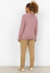 Pink knitted sweater with long sleeves, ribbed neckline, and textured finish, paired with beige slim-fit pants and light-colored shoes.