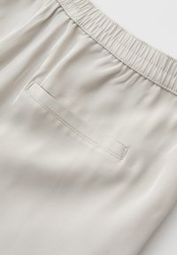 Primo piano di pantaloni con vita elastica beige, una tasca posteriore a filetto singolo e tessuto di cotone liscio.