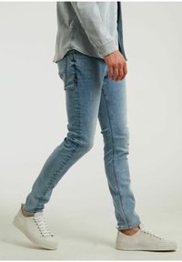 Jasnoniebieskie dopasowane jeansy z denimu, cechujące się czystym wzornictwem i subtelnym blaknięciem. Połączone z białymi, niskimi trampkami.