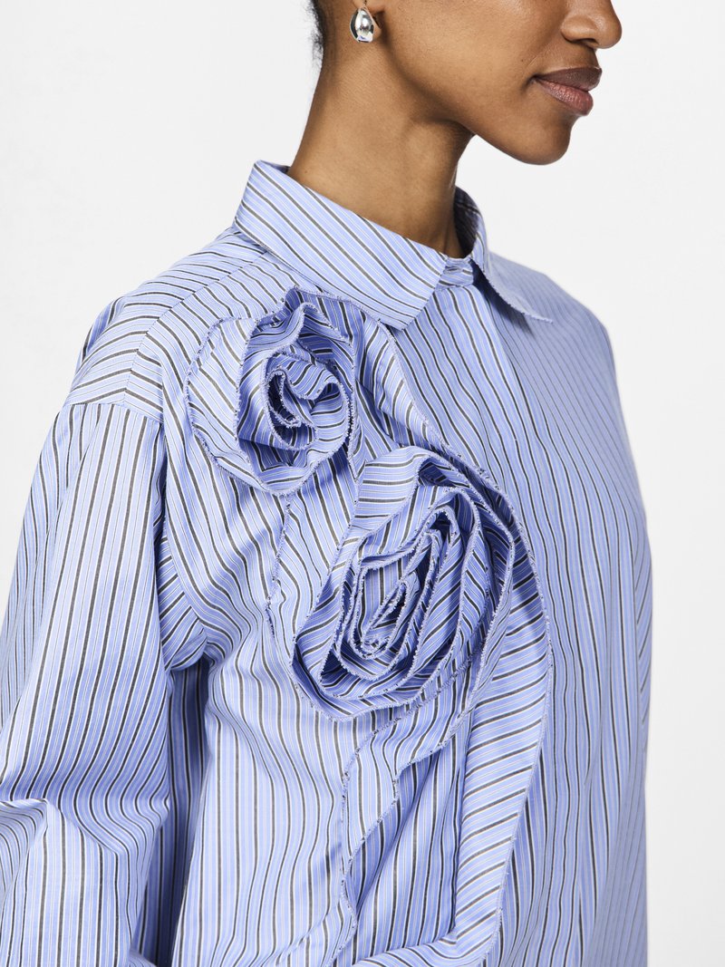 Blauwe gestreepte shirt met grote stoffen rozen aan de linkerkant, met een klassieke kraag en lange mouwen, gemaakt van lichte materialen.