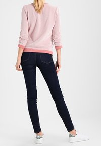 Jeans ajustados azul oscuro combinados con un sudadera texturizada rosa claro y zapatillas blancas con detalles en gris. Ajuste casual, diseño minimalista.