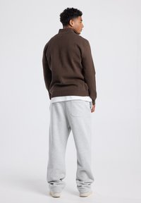Brown knit sweater with a high collar, paired with light gray relaxed-fit sweatpants featuring a back pocket. Smooth textures throughout.
