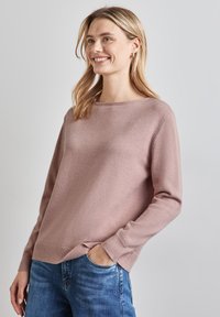 Maglione rosa chiaro in morbido tessuto con scollatura rotonda e maniche lunghe, abbinato a jeans blu. Presenta polsini e orlo a costine.