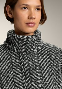 Szary i biały polarowy top z wzorem w zygzak, z wysokim kołnierzem, charakteryzujący się miękką, teksturowaną powierzchnią i luźnym krojem.