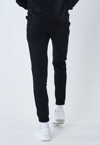 Zwarte fitted joggingbroeken met elastische enkelmanchetten, gemaakt van zachte stof. Gekoppeld met witte sneakers en witte sokken. Geschikt voor casual wear.
