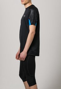 Camiseta atlética negra con acentos azules, hecha de material ligero. Un par de pantalones cortos de compresión negros con costuras texturizadas, hasta la rodilla.